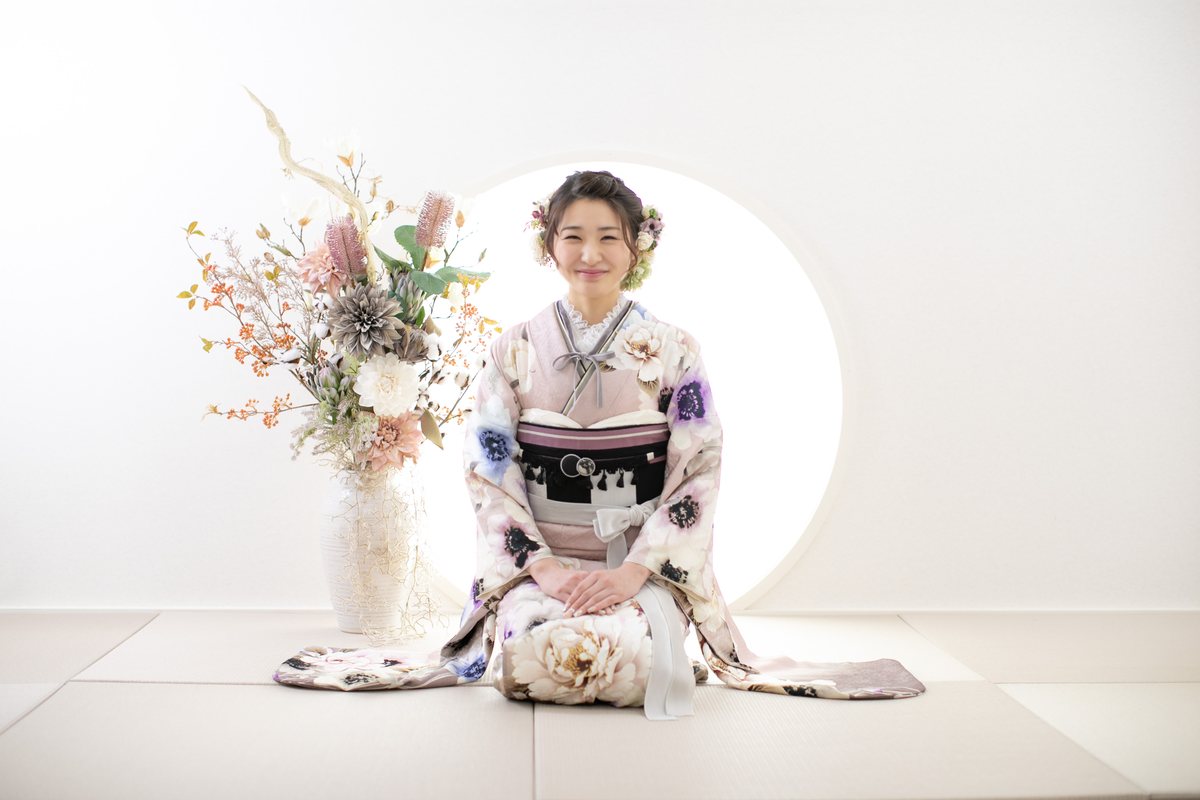 花を背景に振袖姿で正座する成人女性